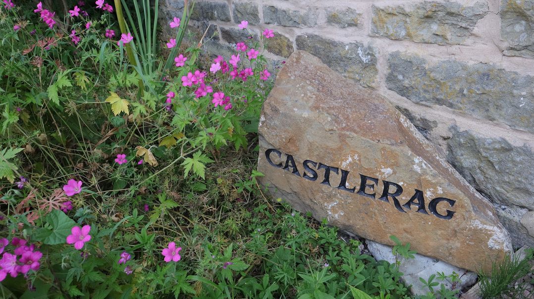 A stone with the name Castlerag surrounded by flowers at Castlerag in Parkend