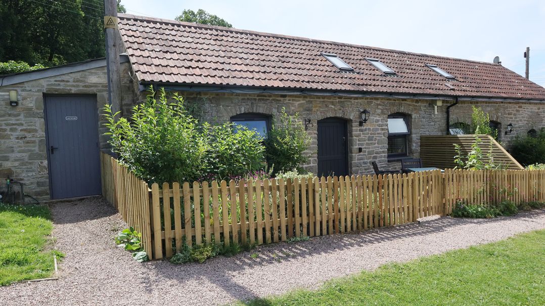 An outdoor view of a stone cottage with a wooden fence at Castle Rag in Parkend