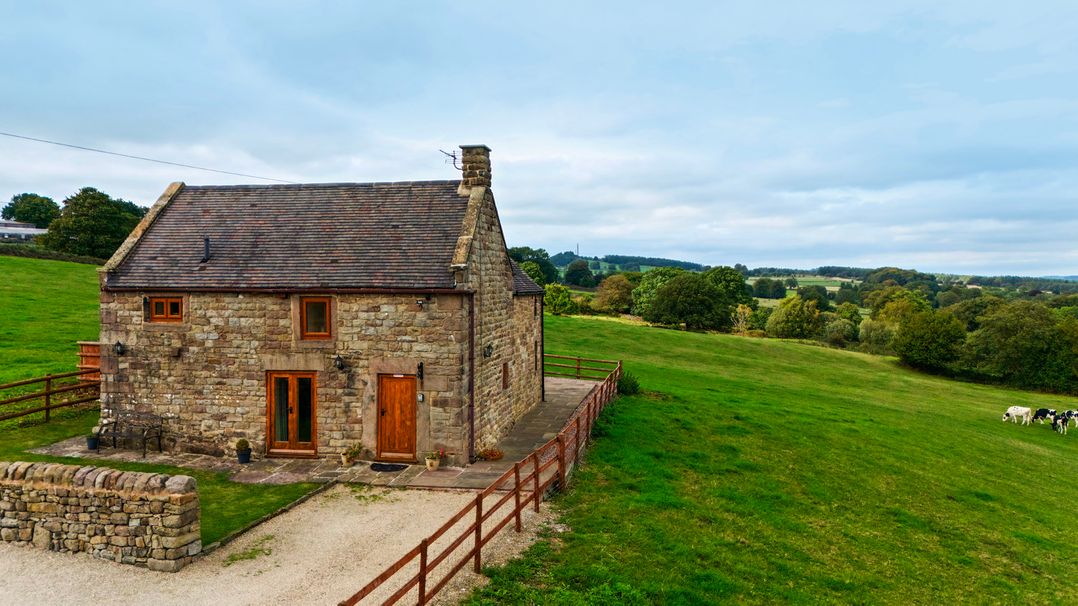 A stone cottage with wooden doors and a fence at Lane Head Cottage Alderwasley near Wirksworth