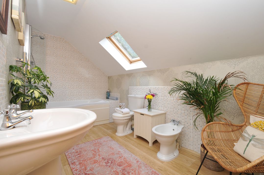 A bathroom with a bathtub, sink, toilet, and chair at The Hayloft in Lostwithiel