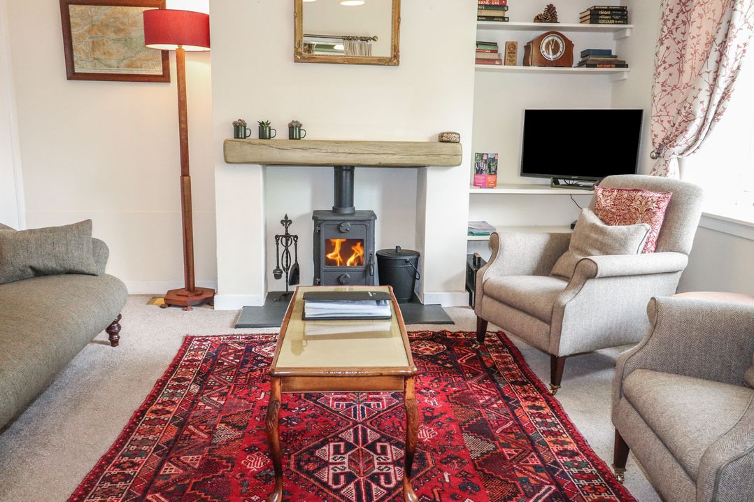 A living room with a fireplace, armchair, and sofa at Branklyn Garden Cottage in Perth