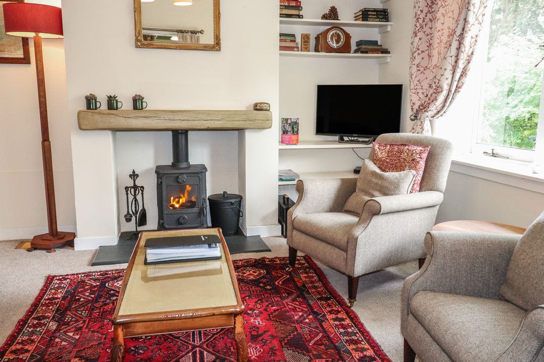 A living room with a fireplace and two chairs at Branklyn Garden Cottage in Perth