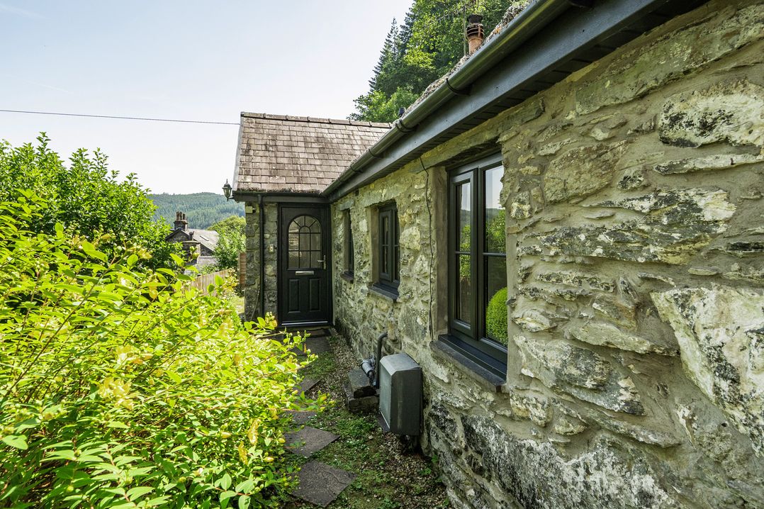 An exterior view of a cottage with stone walls and a pathway at Tyn Y Ffynnon in Betws-Y-Coed