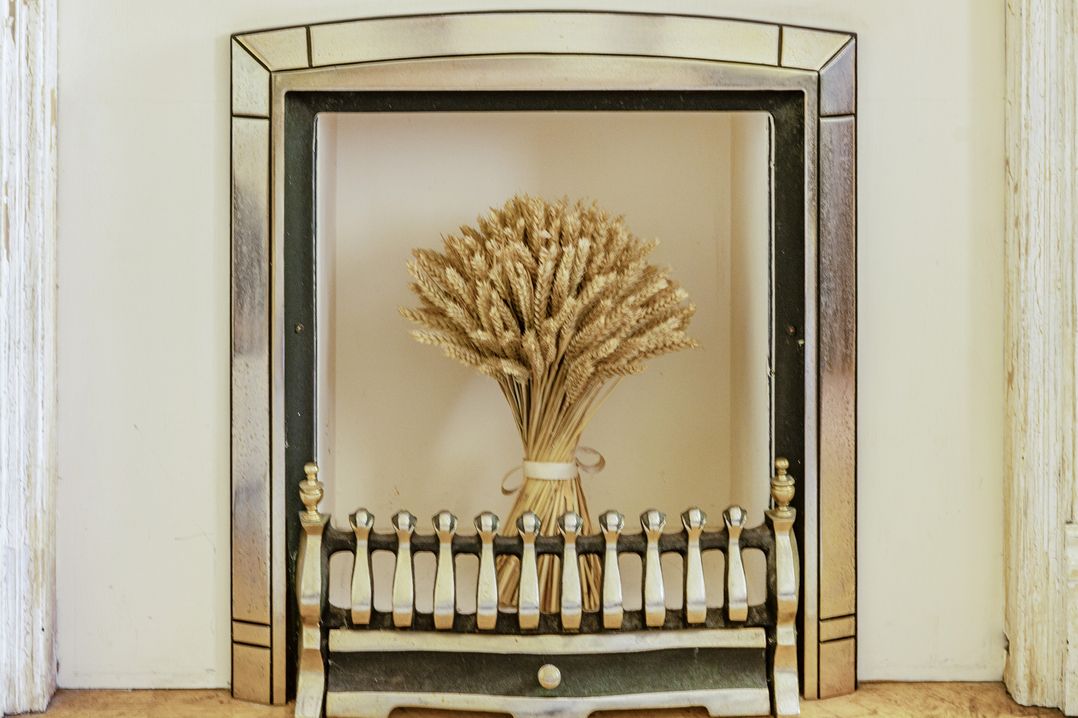A fireplace with a wheat bouquet and fireplace fender at Tyn Y Ffynnon in Betws-Y-Coed
