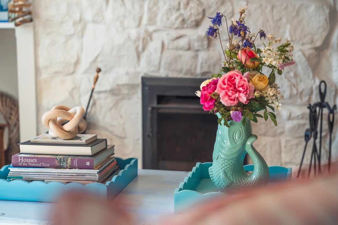 A living room with a vase of flowers and a stack of books at Gerallt in Morfa Nefyn