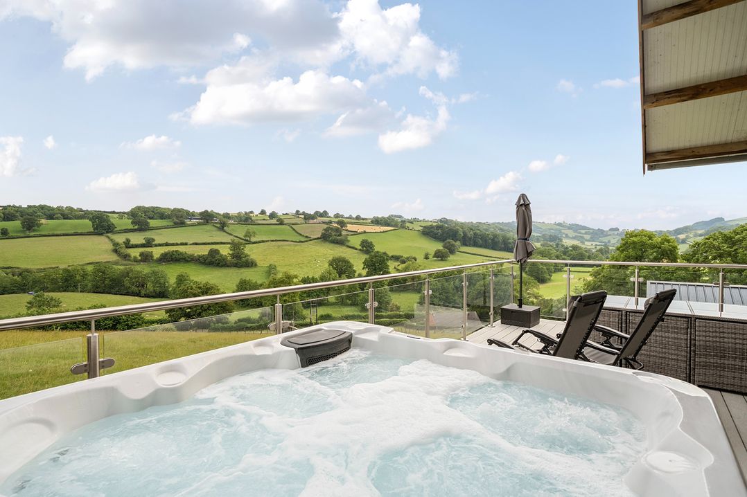 An outdoor area with a hot tub and chairs overlooking the countryside at Bwncath in Garthmyl