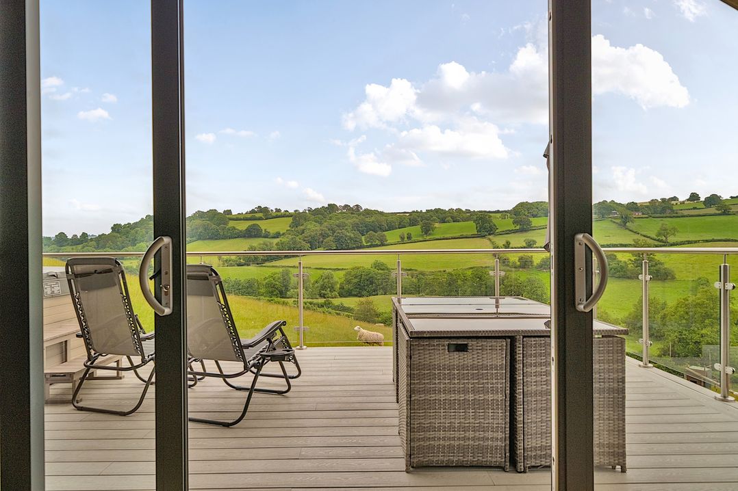 A balcony with chairs and a table overlooking green hills at Bwncath Garthmyl