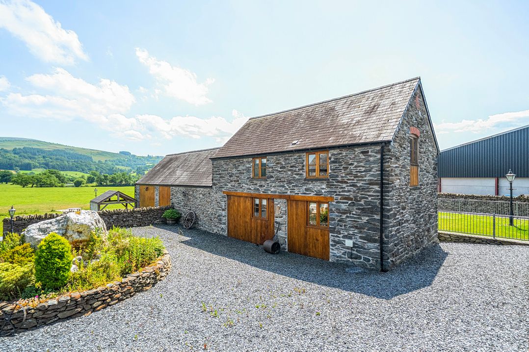 A stone house with wooden doors and a gravel driveway at The Barn in Corwen