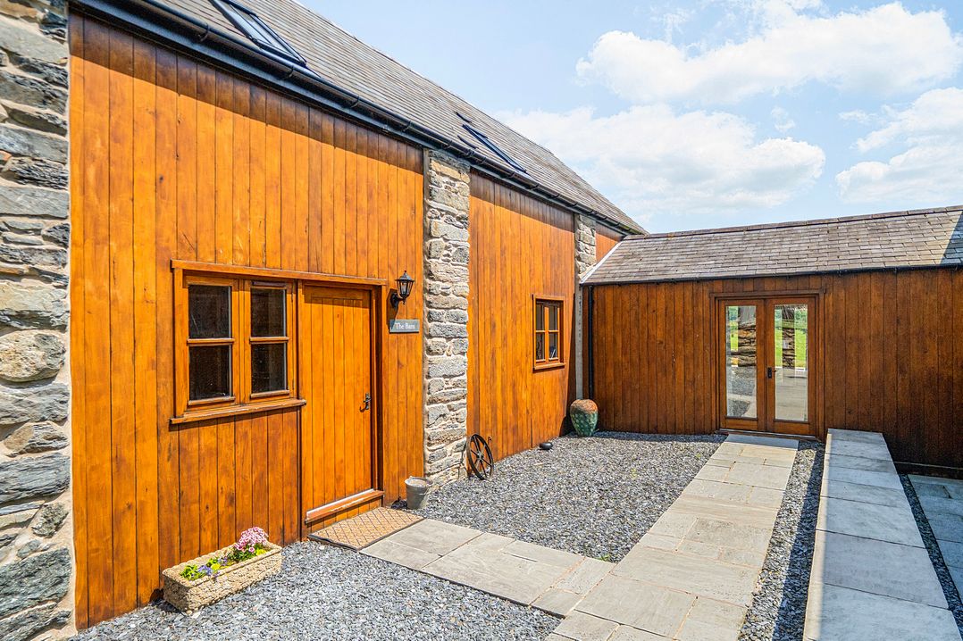 An outdoor view of a wooden structure with a stone wall and pathway at The Barn in Corwen