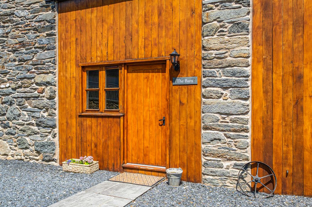 A rustic entrance with wooden door and stone wall at The Barn in Corwen