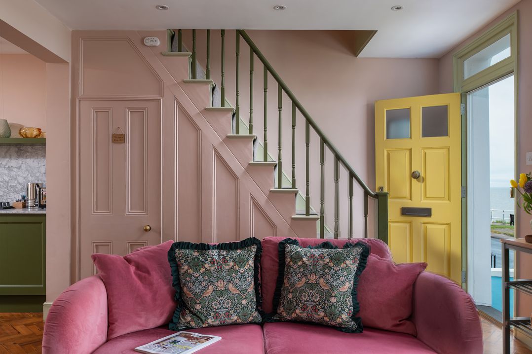 A living room with a pink sofa and yellow door at Astondene, East Cliff in Southwold