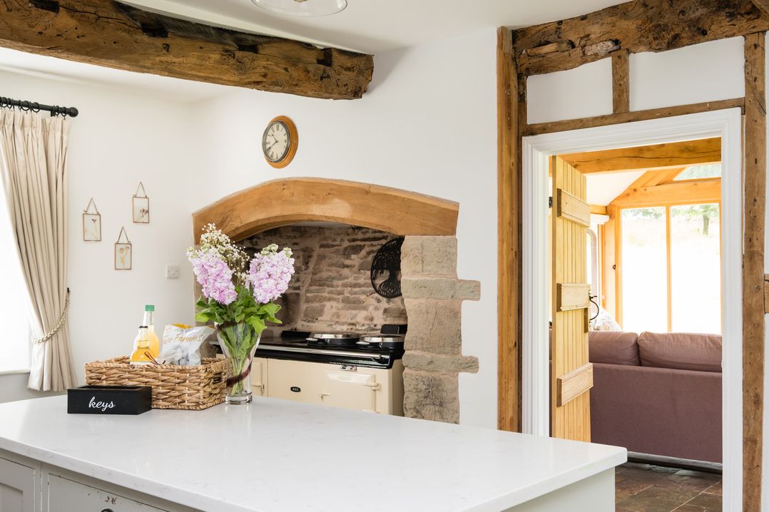 A kitchen with flowers on a counter and an open doorway to a living area at Henhouse Farm Bodenham