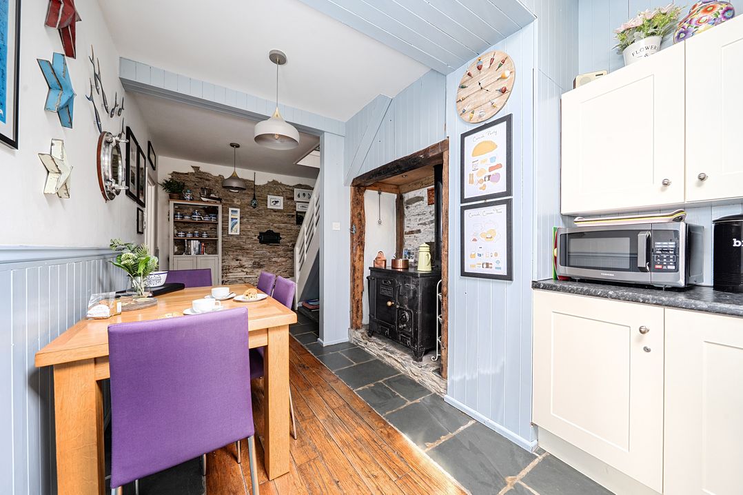 A kitchen with a table and chairs, microwave, and fireplace at Mews Cottage in Tintagel
