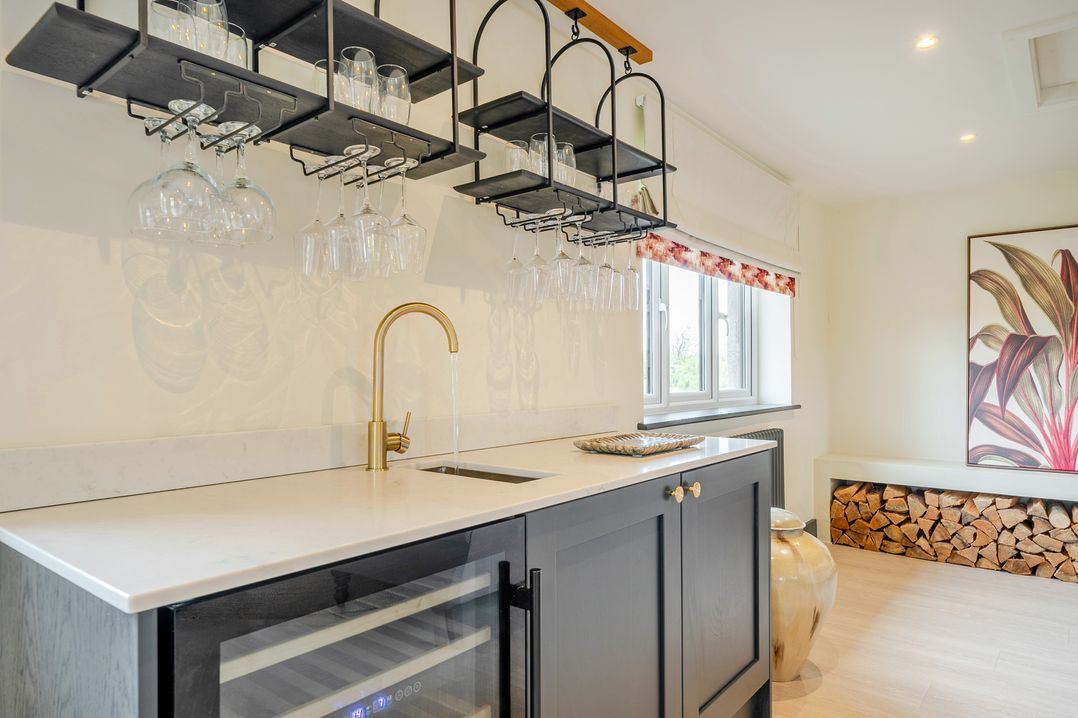 A kitchen with a sink, wine cooler and shelves holding glasses at Bell House Llanfechell