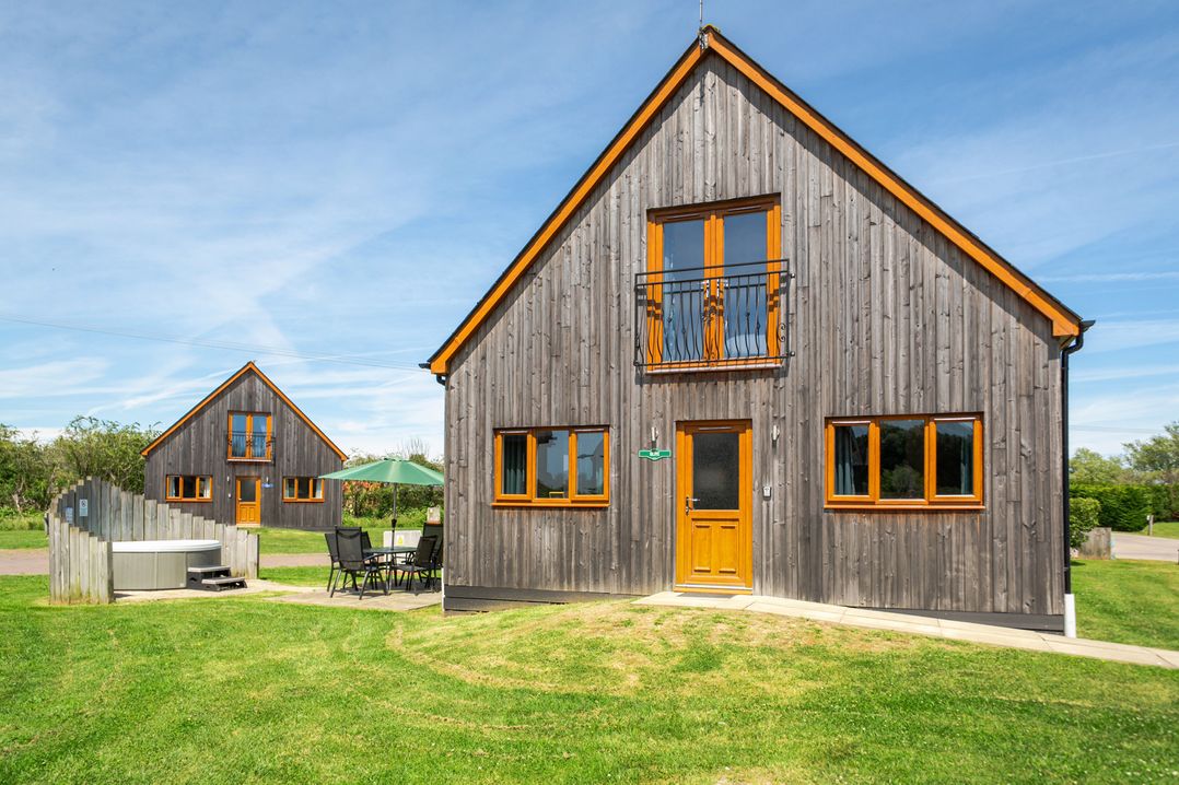 Two wooden houses with a hot tub and chairs in the garden at James Ville Marina Lodge 22 Brigg