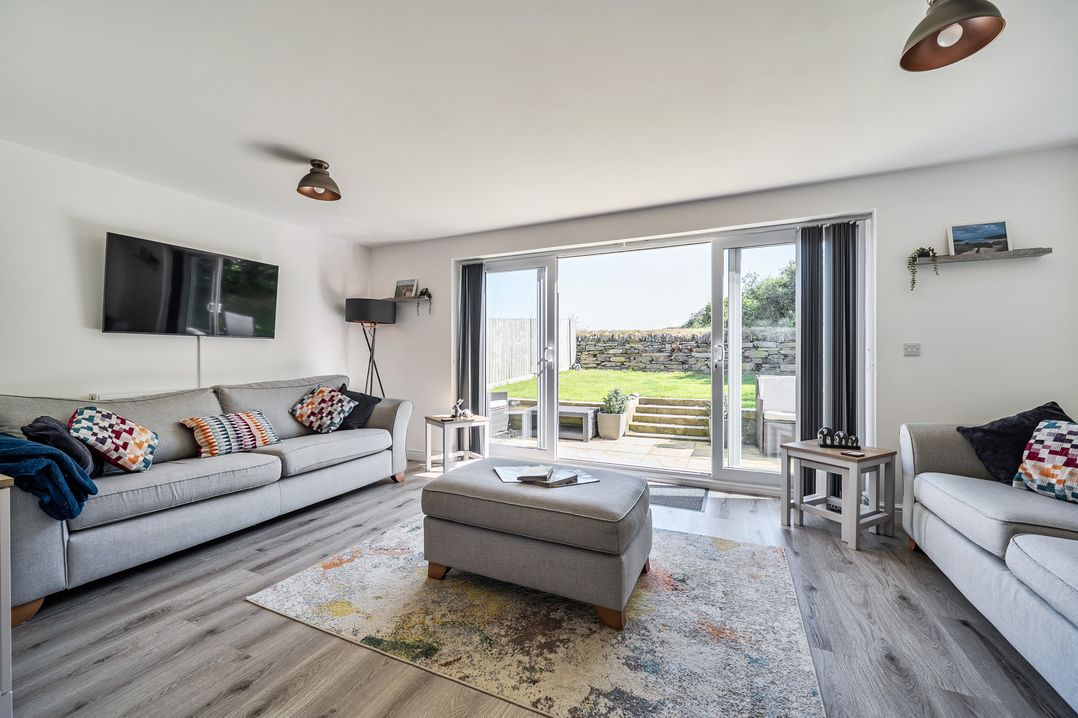 A living room with a sofa and sliding doors to the outdoor area at Buttercup Cottage in St Merryn