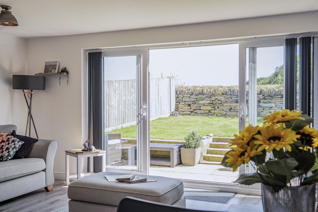 A living room with sliding doors opening to a garden at Buttercup Cottage in St Merryn