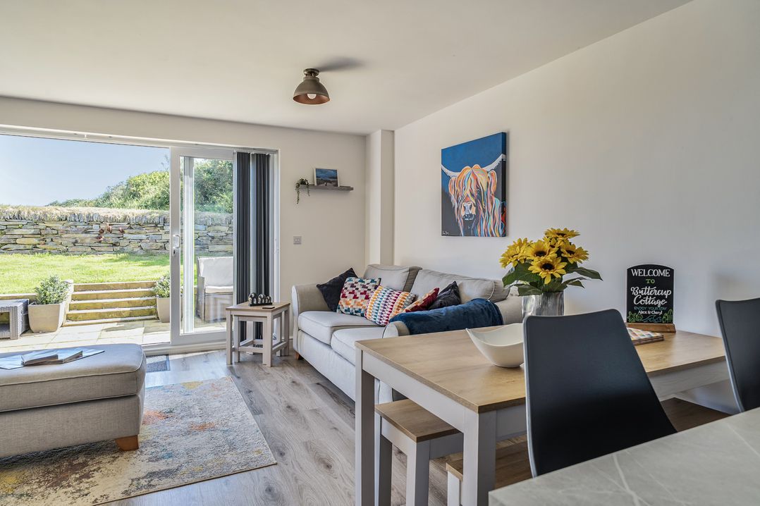 A living room with a sofa and dining table at Buttercup Cottage St Merryn
