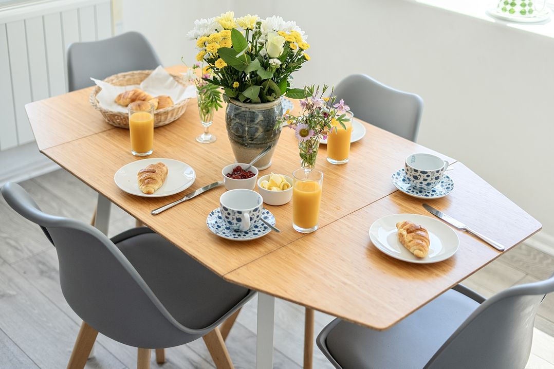 A dining room table set with croissants, juice, and flowers at Brook House Sennen Cove near St Just