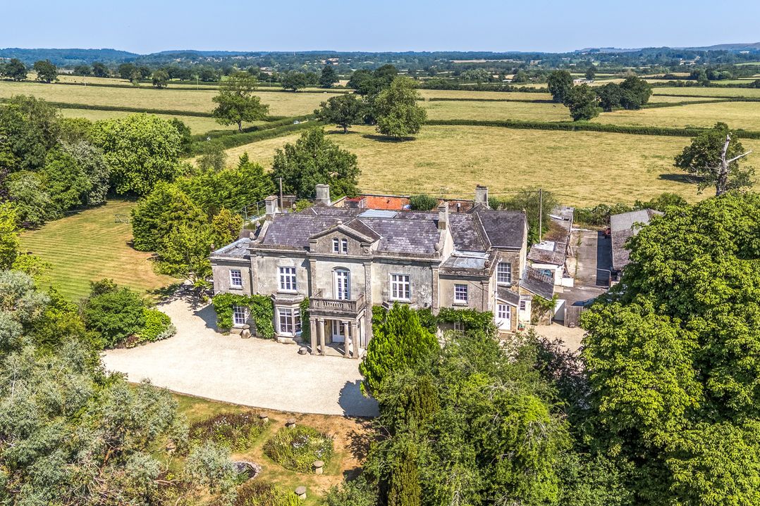 An aerial view of a large house surrounded by fields and trees at Milton Manor in Milton On Stour