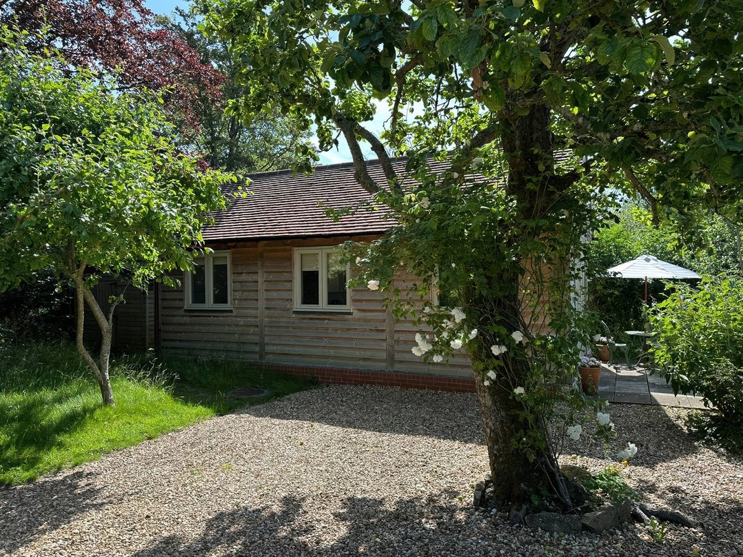 A cottage with trees and a patio area at The Lodge at Mortons in Hankerton