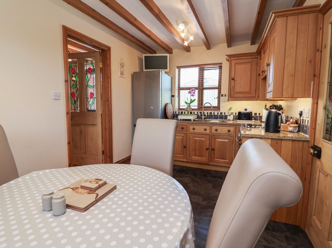 A kitchen with wooden cabinets and a dining table at Ash Farm Cottage Lixwm near Caerwys