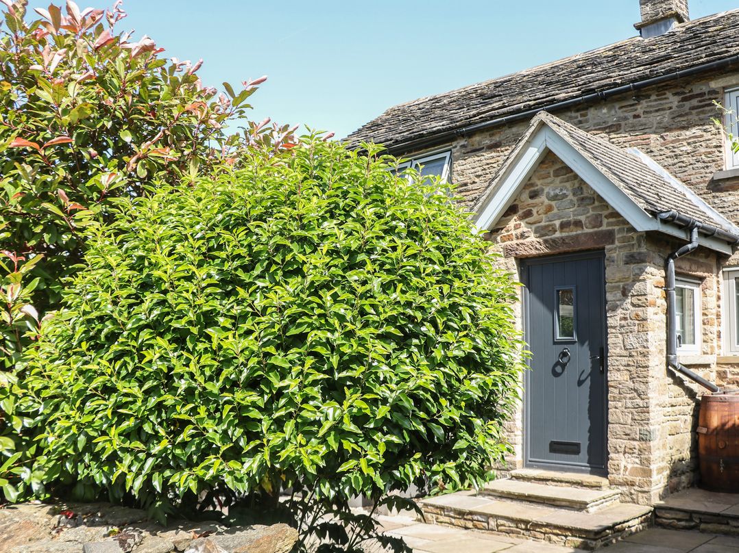 An exterior view of a house with a door and bushes at Overlea Cottage in Hayfield