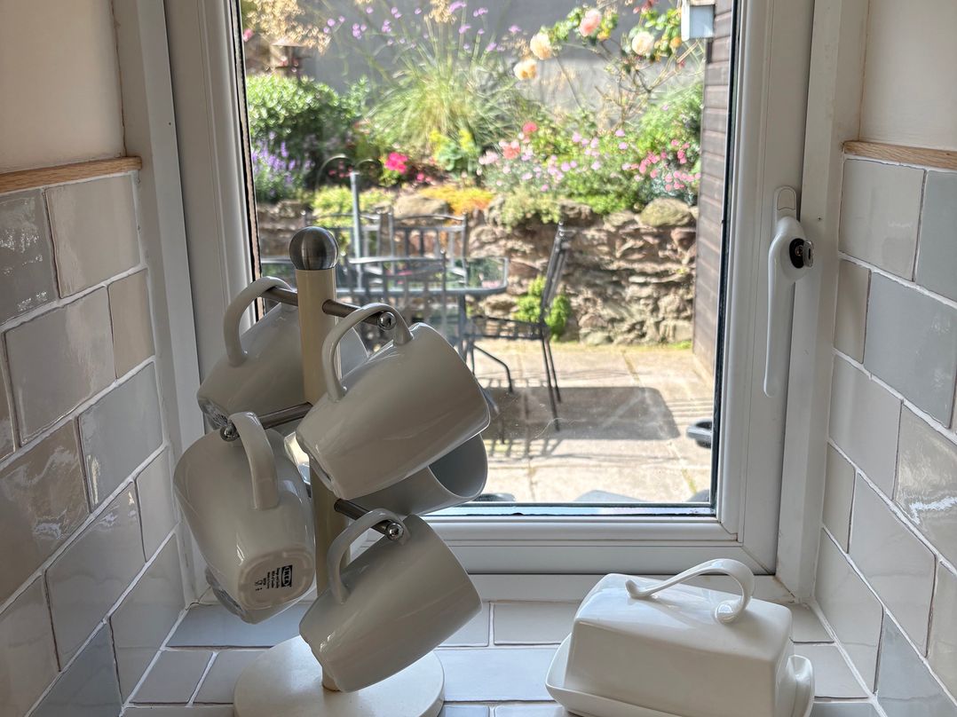 A kitchen with mugs on a holder and a view of a garden at 3 Lowerbourne Terrace in Porlock