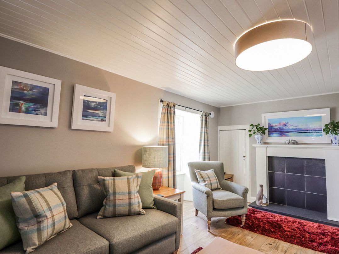 A living room with a sofa, armchair, and fireplace at Craggan Cottage - Balmacara