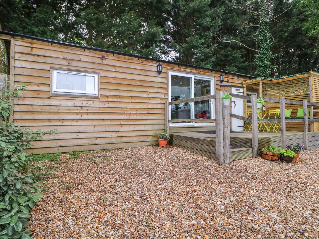 A wooden cabin with a deck at Harvest Lodge in Wineham near Bolney