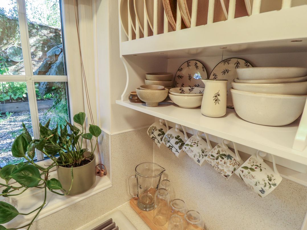 A kitchen with shelf containing dishes and mugs at Hangmans cottage in Horncastle