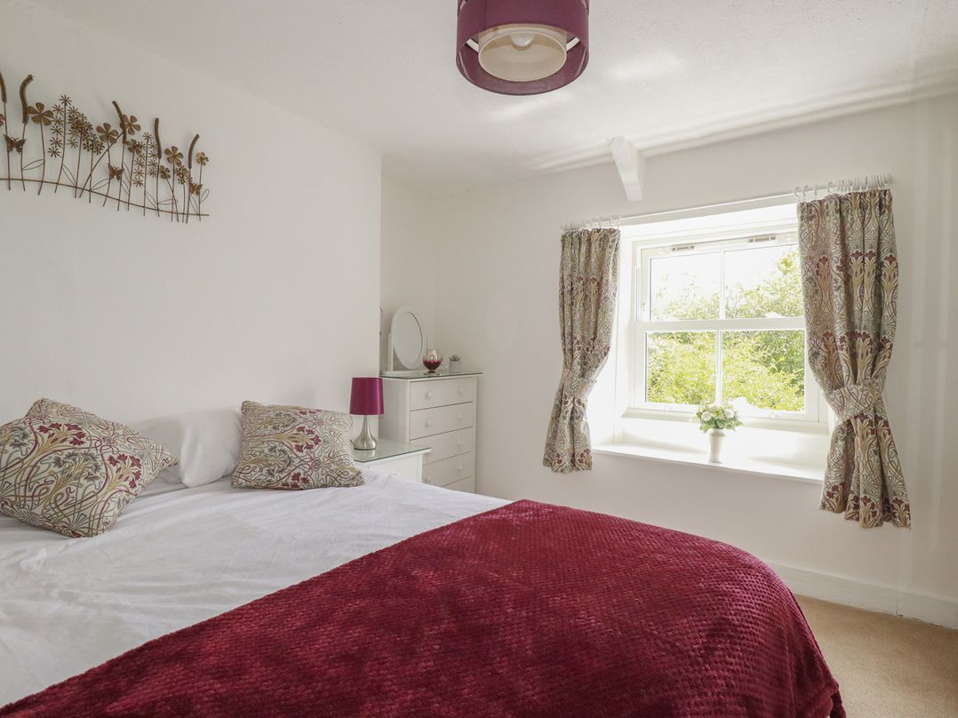 A bedroom with a bed, lamp, and window at Gwynn Cottage St Mabyn