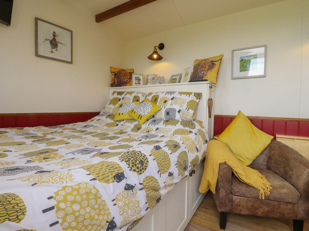 A bedroom with a bed and chair at The Herdsman Luxury Shepherds Hut in Barnoldswick