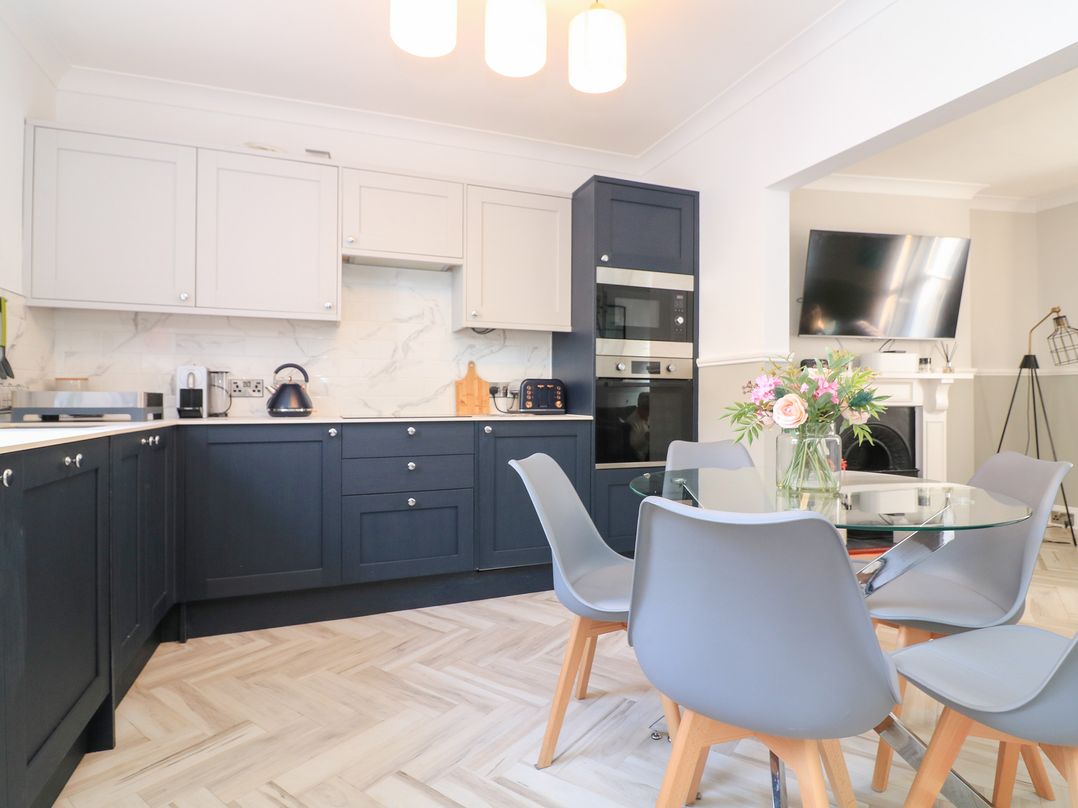 A kitchen with blue and white cabinets a glass dining table with gray chairs and a wall-mounted TV at Green Retreat in Dartmouth