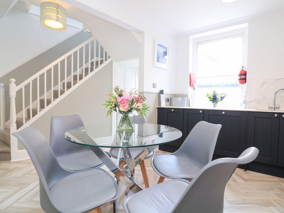 A dining area with gray chairs around a glass table and flowers in a vase near a staircase at Green Retreat in Dartmouth