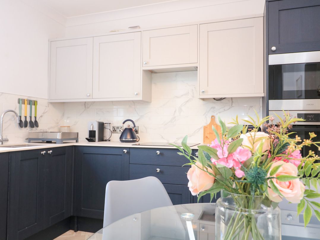 A kitchen with dark lower cabinets and light upper cabinets a kettle coffee machine utensils and flowers on a glass table at Green Retreat in Dartmouth