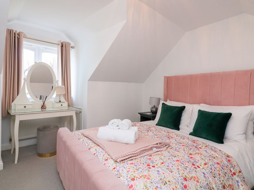 A bedroom with a pink bed, floral bedding, green pillows, a white dressing table with an oval mirror and a stool at Green Retreat in Dartmouth