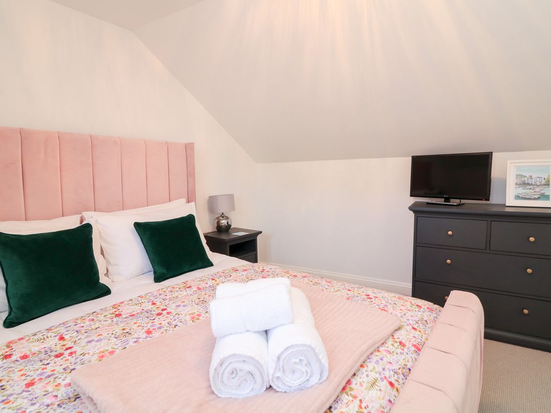 A bedroom with a bed with pink headboard green pillows and rolled white towels on top at Green Retreat in Dartmouth