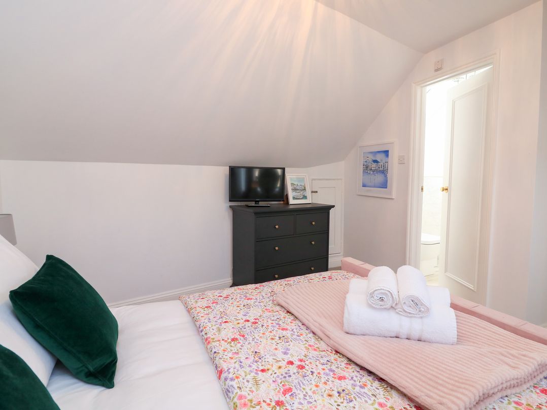 A bedroom with a bed featuring green pillows and floral bedding a black dresser with a TV and framed pictures and an open door leading to a bathroom at Green Retreat in Dartmouth