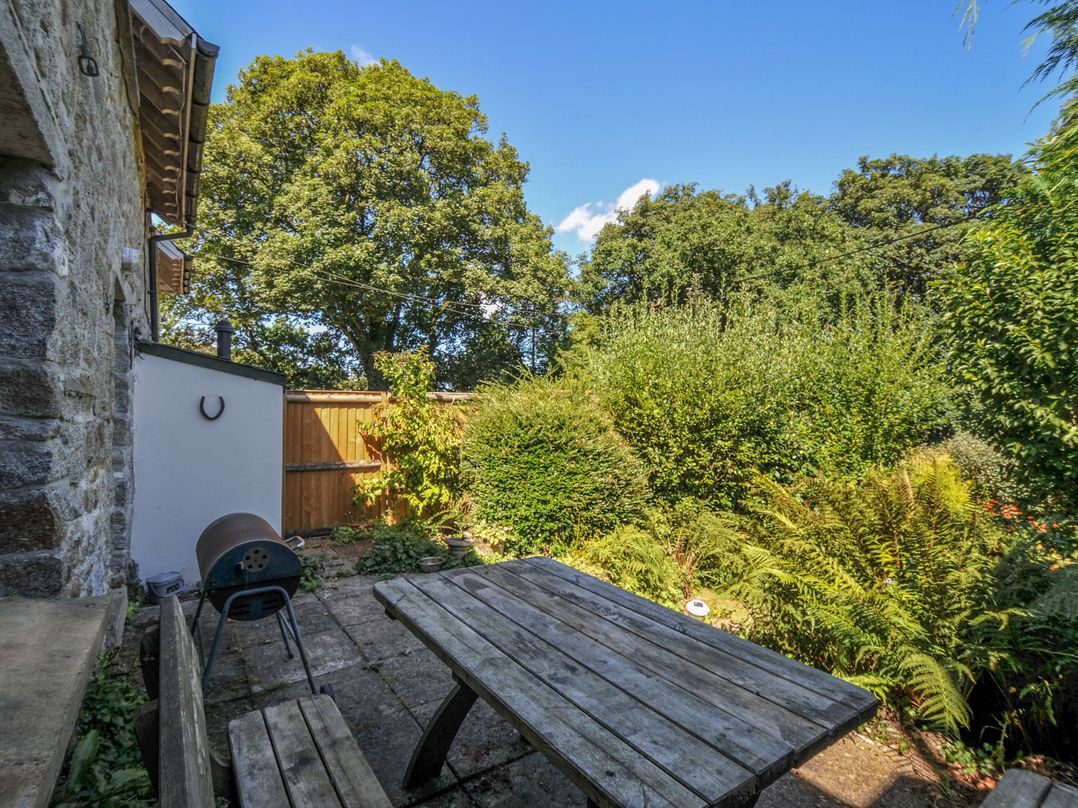A garden with a table, chairs, and barbecue at The Mews in Blisland