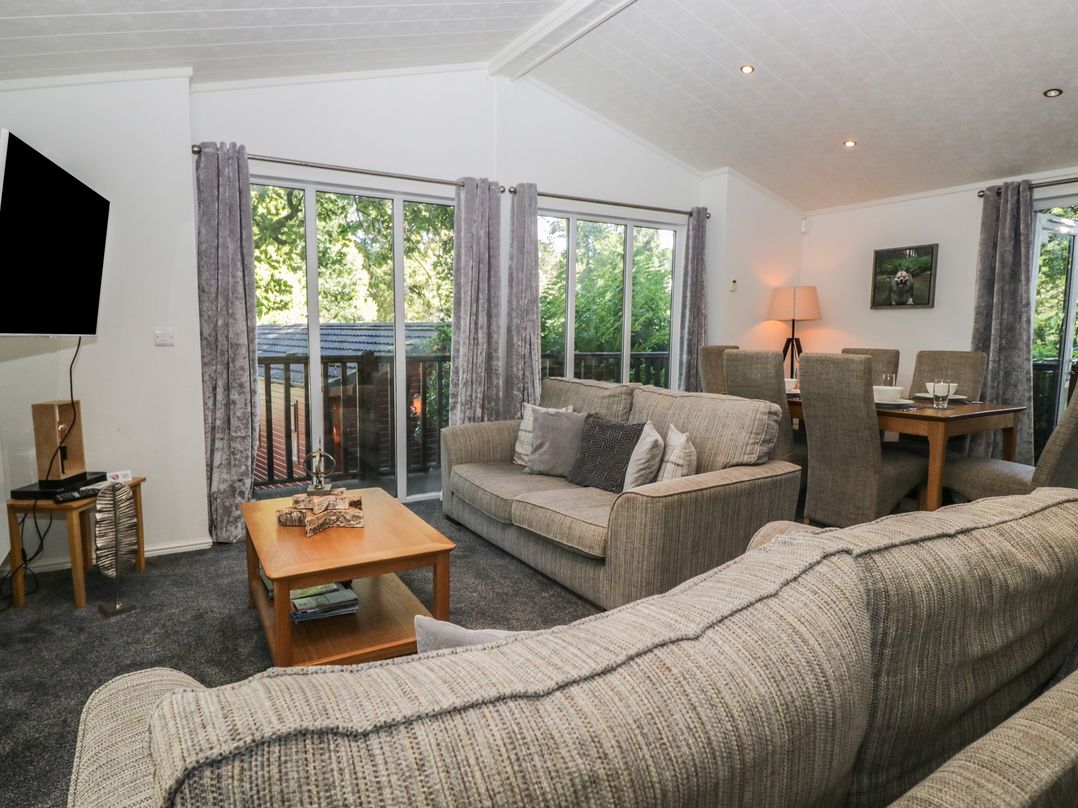 A living room with a sofa, tv, and dining area at Treetops, Beech Hill 13, Fallbarrow Park near Bowness-On-Windermere