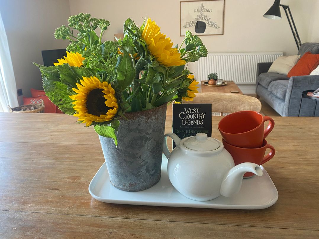A tray with sunflowers in a pot, a teapot, red cups and a book in a living room at Church Farm Dairy Cadbury near Thorverton