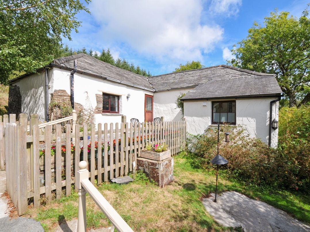 A cottage surrounded by a fence and flower bed at Windbury Cottage in Hartland