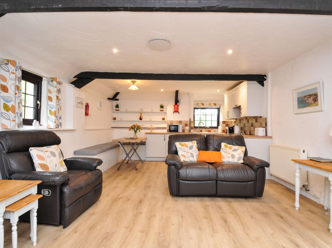 A living room with seating and kitchen area at Windbury Cottage in Hartland