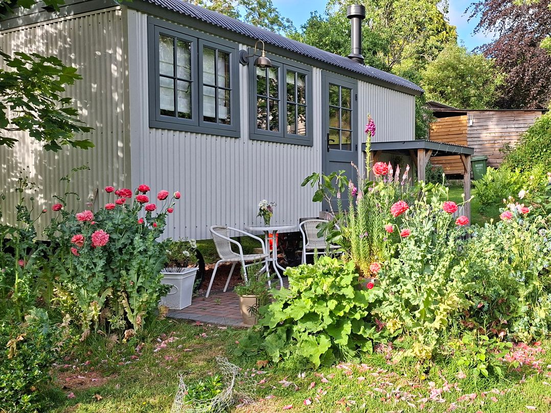A garden with flowers and seating near a small building at Evendine Hut @ Evendine Cottage, Colwall, Herefordshire
