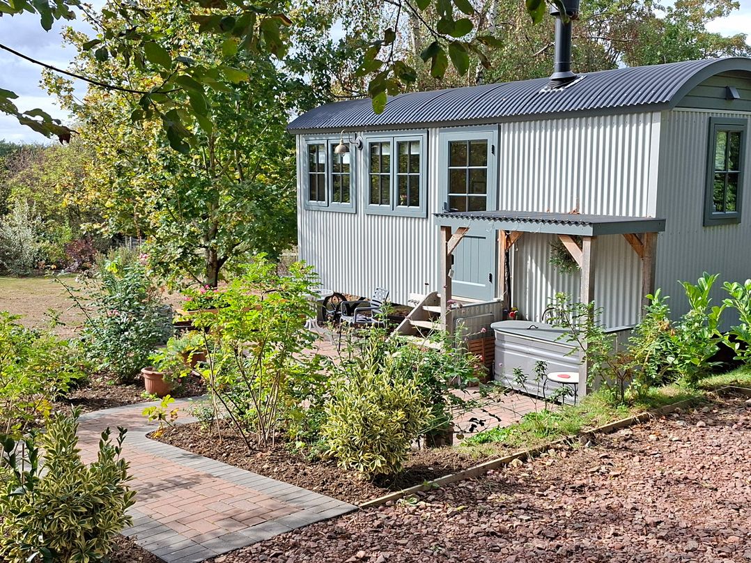 A shed with windows and chimney surrounded by garden at Evendine Hut @ Evendine Cottage, Colwall, Herefordshire