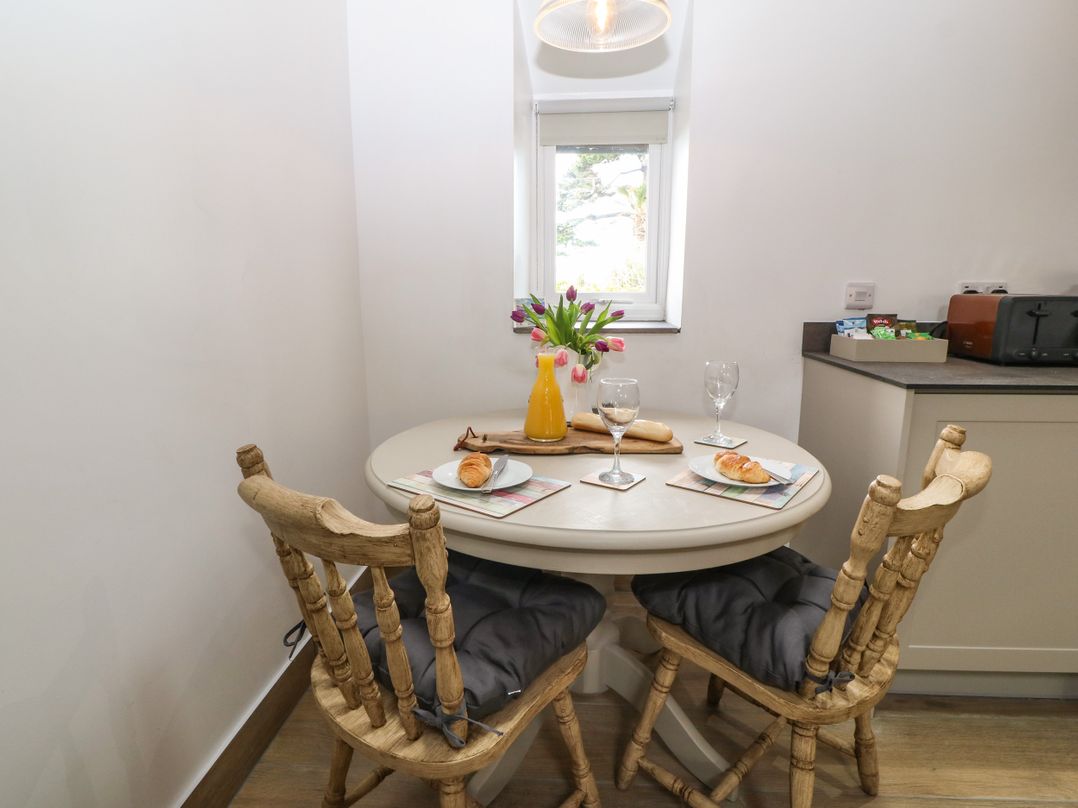 A breakfast nook with a round table two wooden chairs with cushions orange juice croissants and flowers at Y Stabl in Dyffryn Ardudwy
