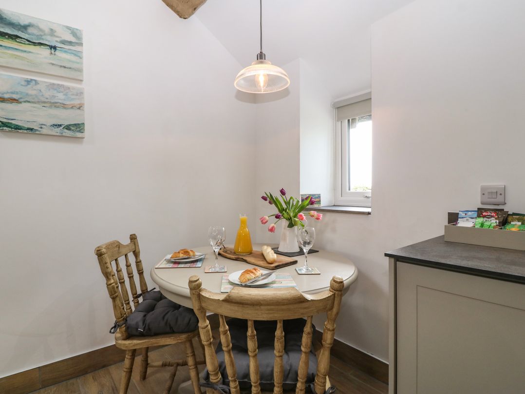 A dining area with a round table set with croissants orange juice and flowers two wooden chairs and paintings on the wall at Y Stabl in Dyffryn Ardudwy