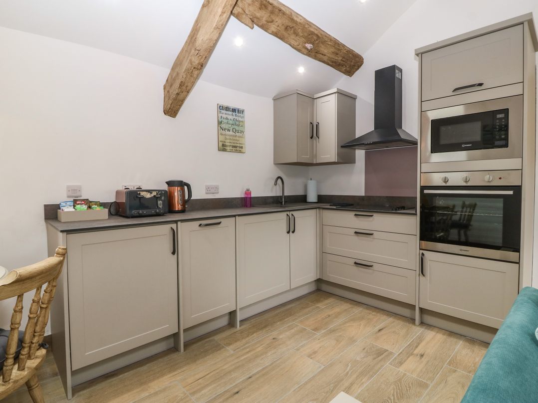 A kitchen with beige cabinets a black countertop a toaster kettle microwave and built in oven at Y Stabl in Dyffryn Ardudwy