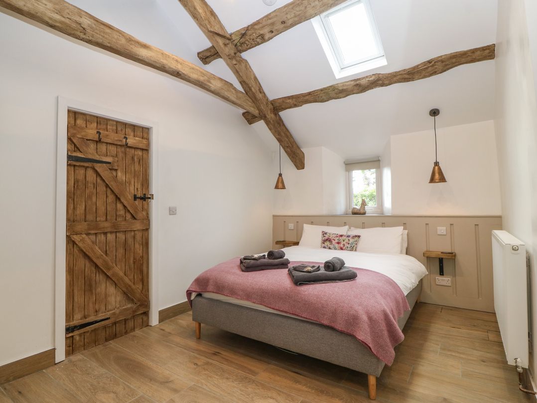 A bedroom with a bed with folded towels on a pink blanket wooden door and exposed wooden beams at Y Stabl in Dyffryn Ardudwy